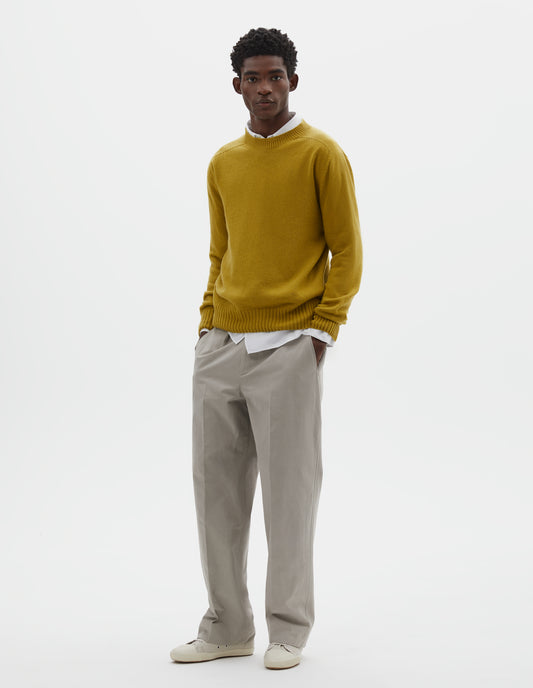Full body image, front view of model wearing yellow crew neck jumper with seamless finish and contrast ribs on neck, cuffs and hem. Styled over white cotton shirt, with grey trousers and off white canvas trainers.