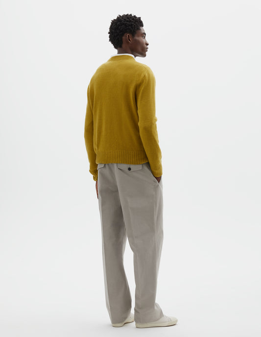 Full body image, back view of model wearing yellow crew neck jumper with seamless finish and contrast ribs on neck, cuffs and hem. Styled over white cotton shirt, with grey trousers and off white canvas trainers.