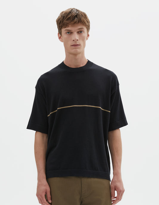 Cropped body image, front view of model wearing regular, generous fit, black knitted t-shirt with deep rib crew neck, set in sleeves and single dark beige stripe across body. Styled with khaki green trousers.