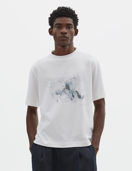 Cropped body image, front view of model wearing white relaxed, boxy crew neck t-shirt with dark grey drawing print. Styled with dark blue trousers.