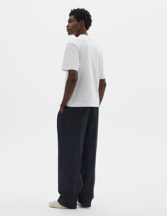 Full body image, back view of model wearing white relaxed, boxy crew neck t-shirt. Styled with dark blue trousers and beige canvas trainers.