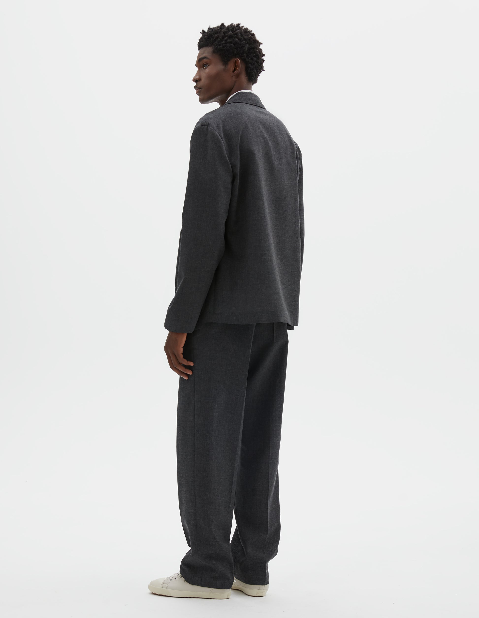 Full body image, back view of model wearing grey crisp wool blazer. Styled with matching grey trousers and beige canvas trainers. 