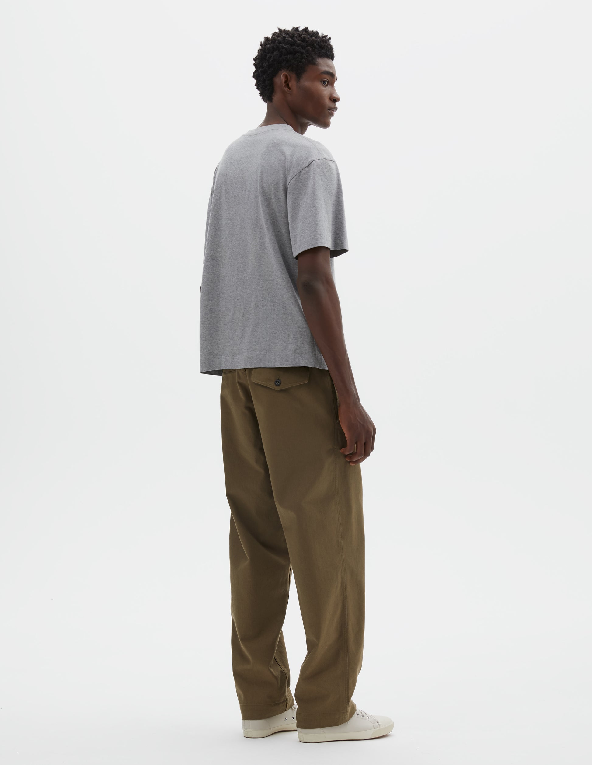 Full body image, back view of model wearing grey cotton short sleeve t-shirt. Styled with green trousers and beige canvas trainers.