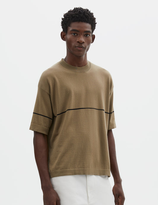 Cropped body image, front view of model wearing regular, generous fit, dark beige knitted t-shirt with deep rib crew neck, set in sleeves and single black stripe across body. Styled with white trousers.