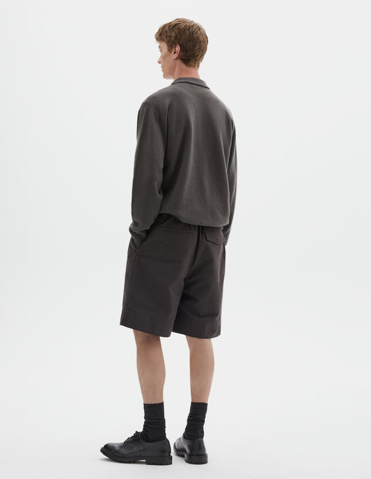 Full body image, back view of model wearing dark grey merino cashmere polo shirt with dropped sleeve and rib collar, cuffs and hem. Styled with brown shorts, black socks and black leather brogues.