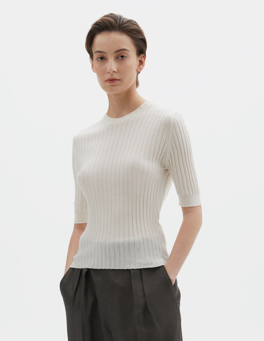 Cropped body image, front view of model wearing beige knitted ribbed t-shirt with round neck and fine rib sleeve cuffs. Styled with greyish-green trousers.