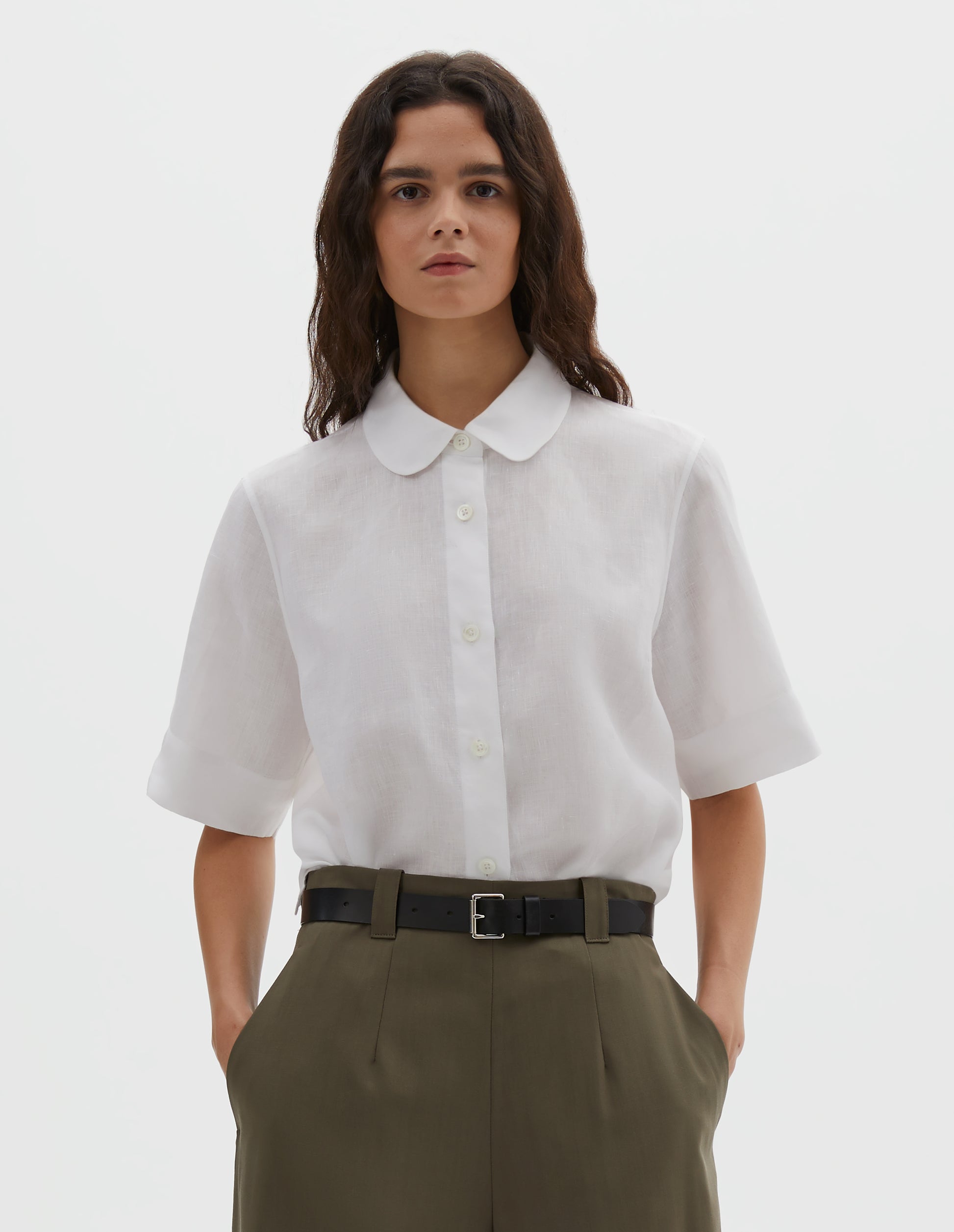 Cropped body image, front view of female model wearing black leather belt with silver buckle and black leather strap. Styled with white shirt and green trousers.