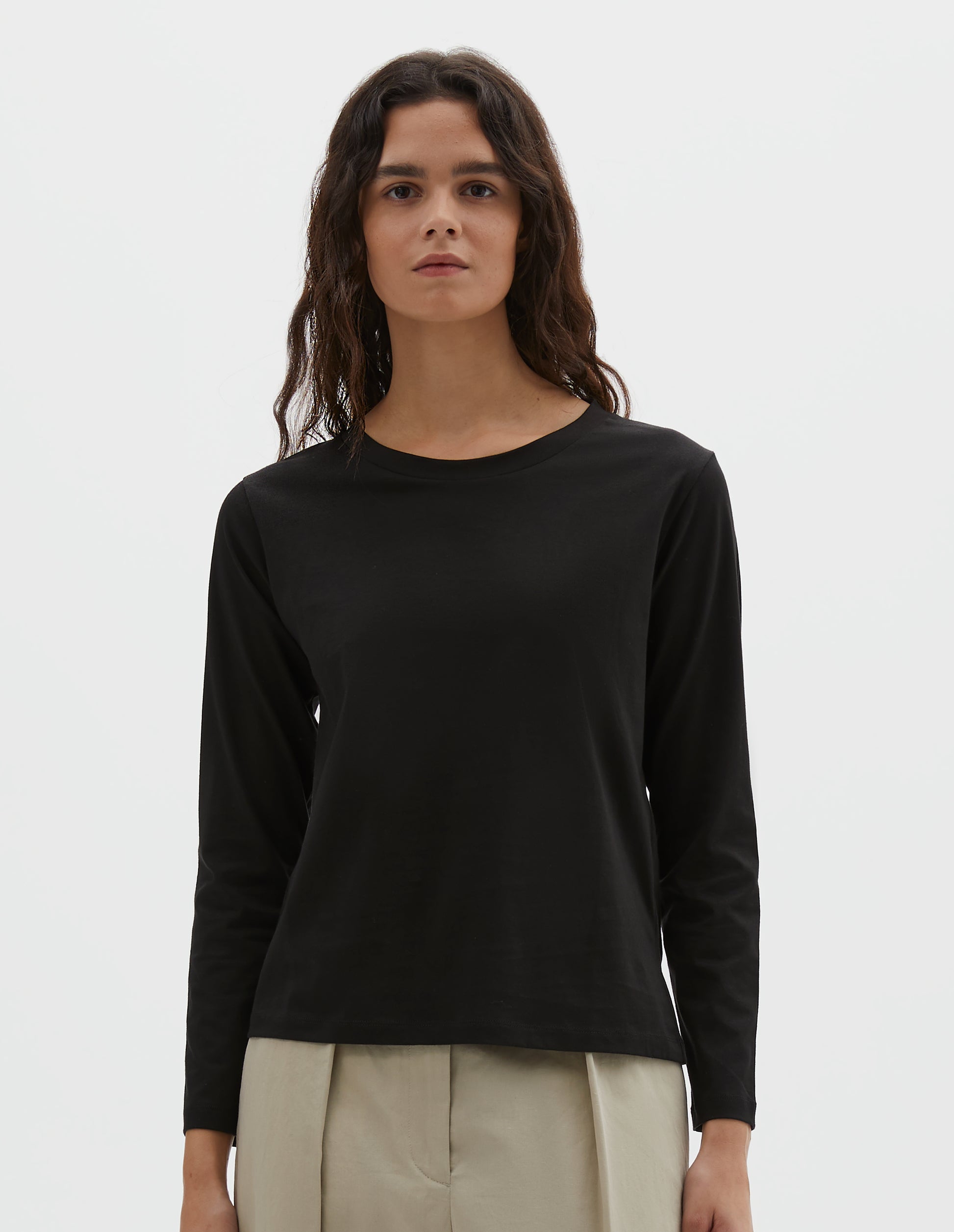 Cropped body image, front view of model wearing black cotton wide neck long sleeve with boxy cut. Styled with beige pleated trousers.