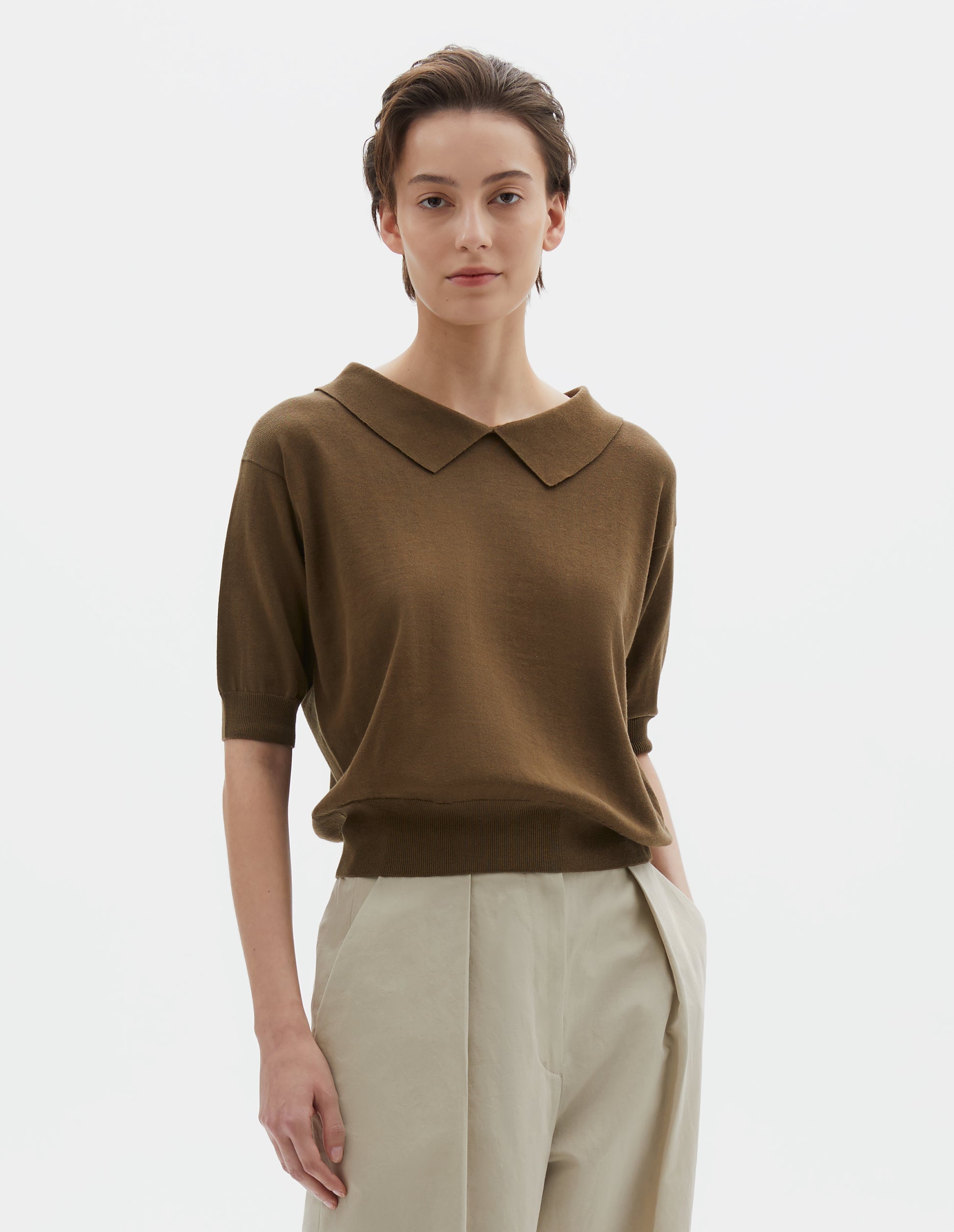 Cropped image, front view of model wearing regular fit green split collar knitted t-shirt with ribbed cuffs and hem. Styled with beige trousers. 