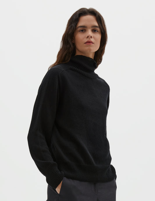 Cropped body image, front view of model wearing black linen cotton roll neck jumper with long saddle sleeves and contrast rib on neck, cuffs and hem. Styled with black trousers.
