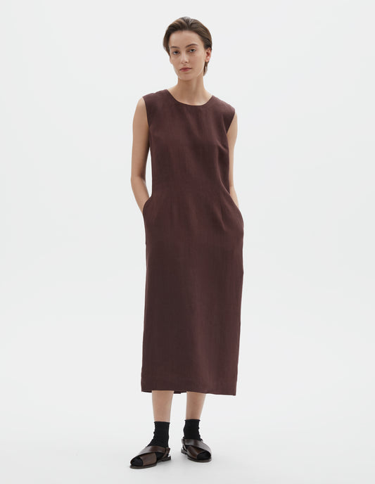 Full body image, front view of model wearing brown regular cut midi length sleeveless dress with side pockets. Styled with black socks and dark brown leather sandals.