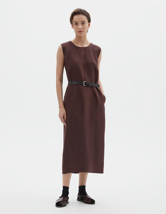 Full body image, front view of model wearing brown regular cut midi length sleeveless dress with side pockets. Styled with black leather belt, black socks and dark brown leather sandals.