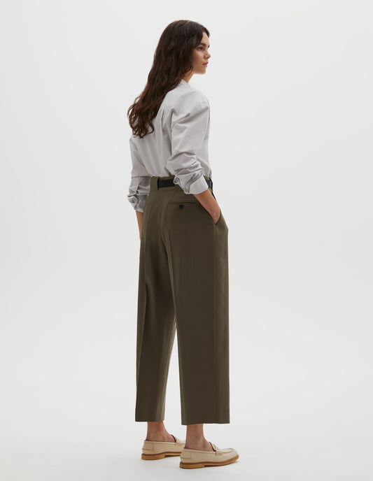 Full body image, back view of model wearing brown wool trousers, grown-on waistband with large belt loops and a button-through jet back pocket and horn button. Styled with grey shirt , dark brown belt and beige shoes.