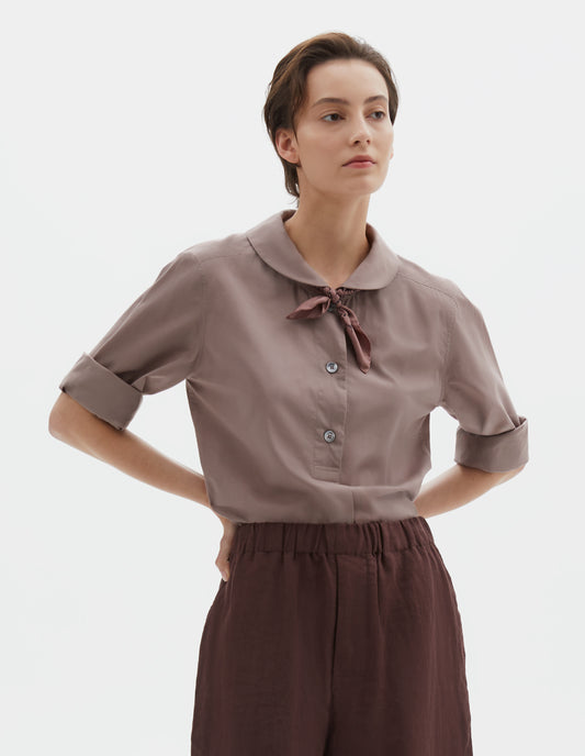 Cropped body image, front view of model wearing a pink bandana under the collar. Styled with a greyish pink round collar shirt and brown elasticated waist shorts.