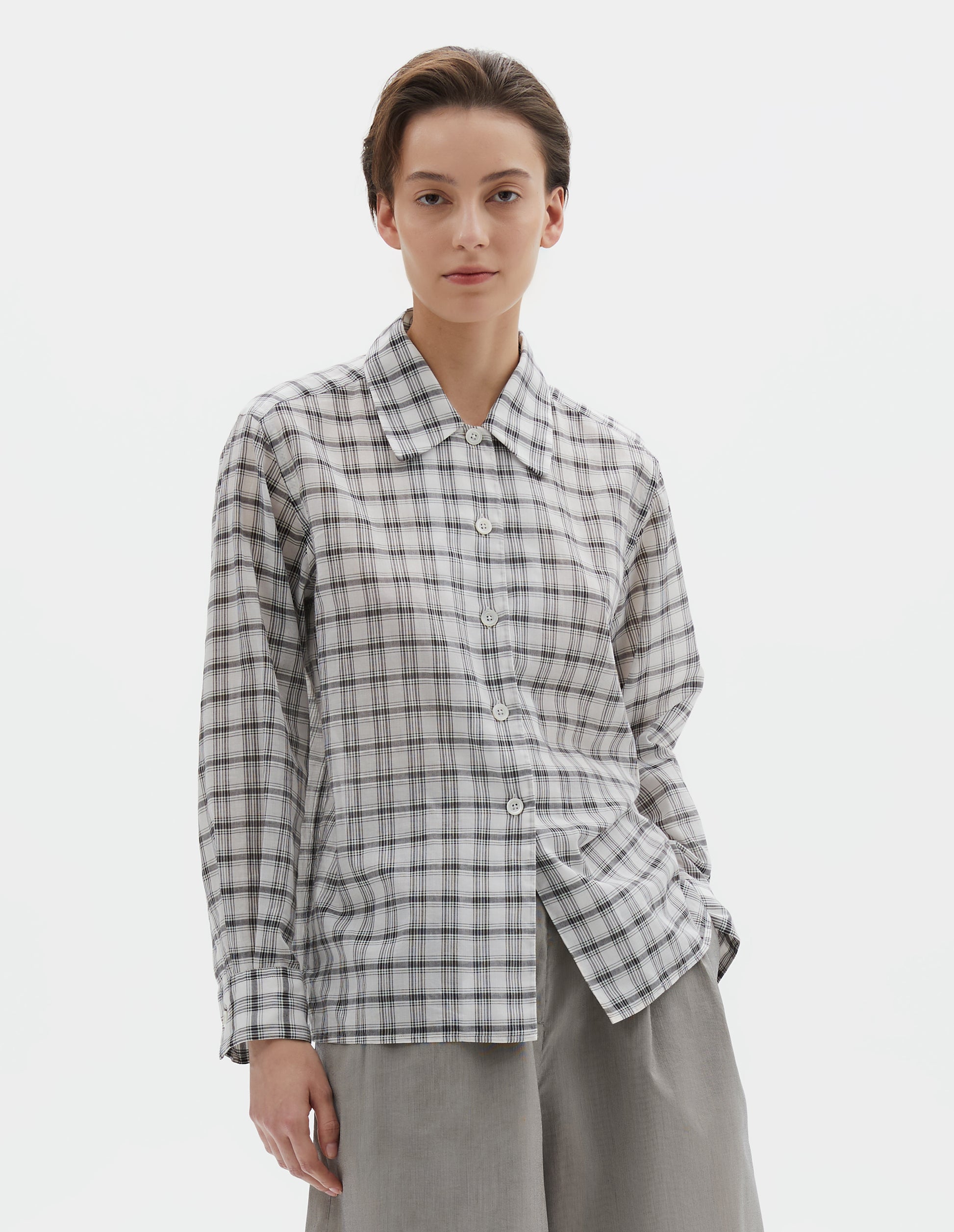 Cropped body image, front view of model wearing white with black check shirt with a curved collar, side split hem. Styled with black and beige fine stripe shorts.
