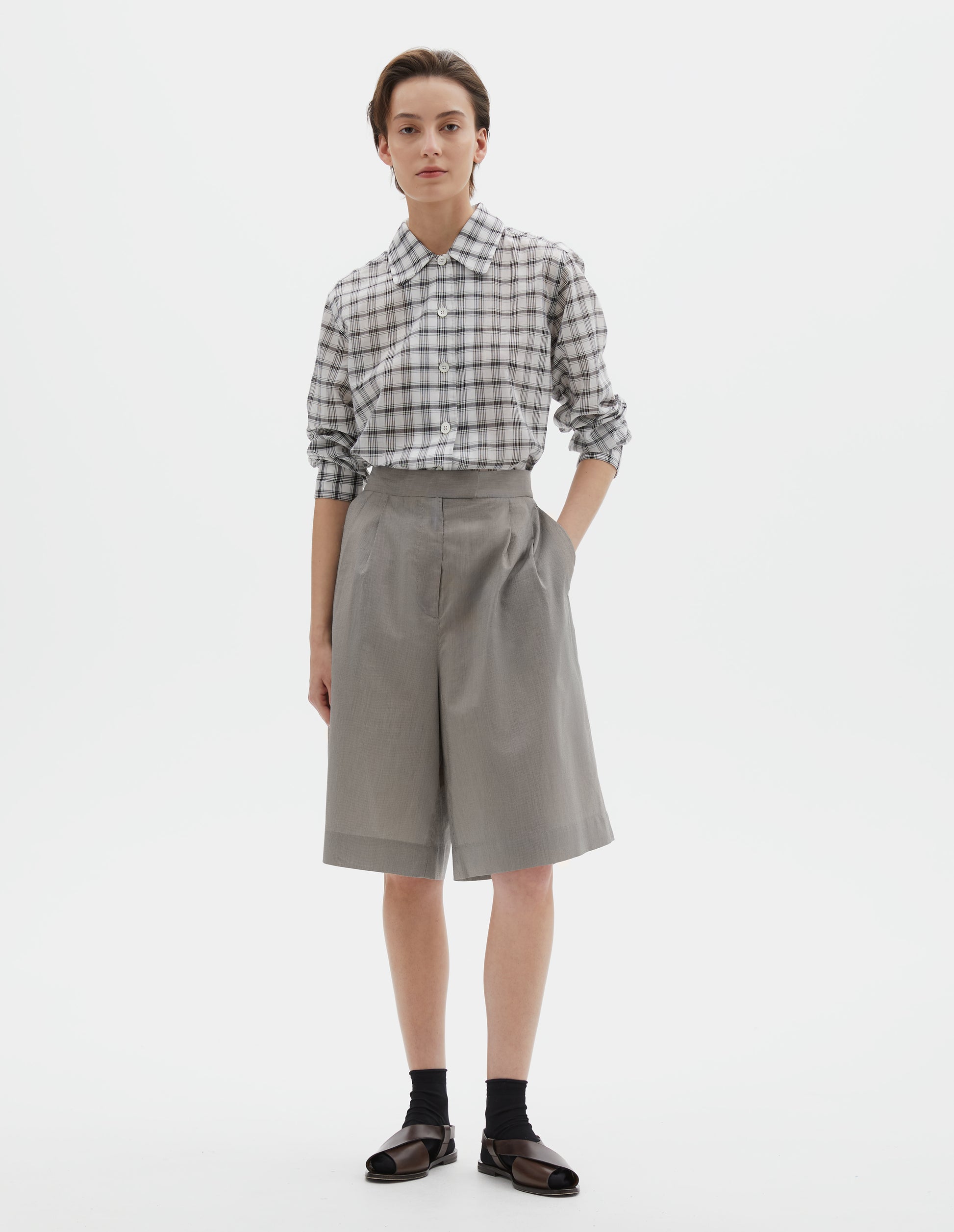 Full body image, front view of model wearing black and cream stripe regular cut knee length shorts with double pleats, hook and bar tab fastening waistband, zip fly and slant side pockets. Styled with white shirt with black check, black socks and brown leather sandals.