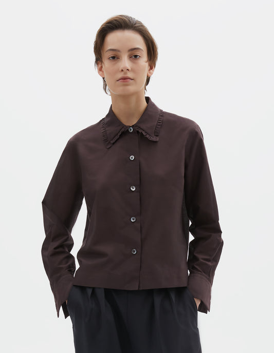Cropped body image, front view of model wearing dark red cotton silk frilled collar long sleeve shirt, with mother of pearl button closure. Styled with dark navy wide leg trousers.