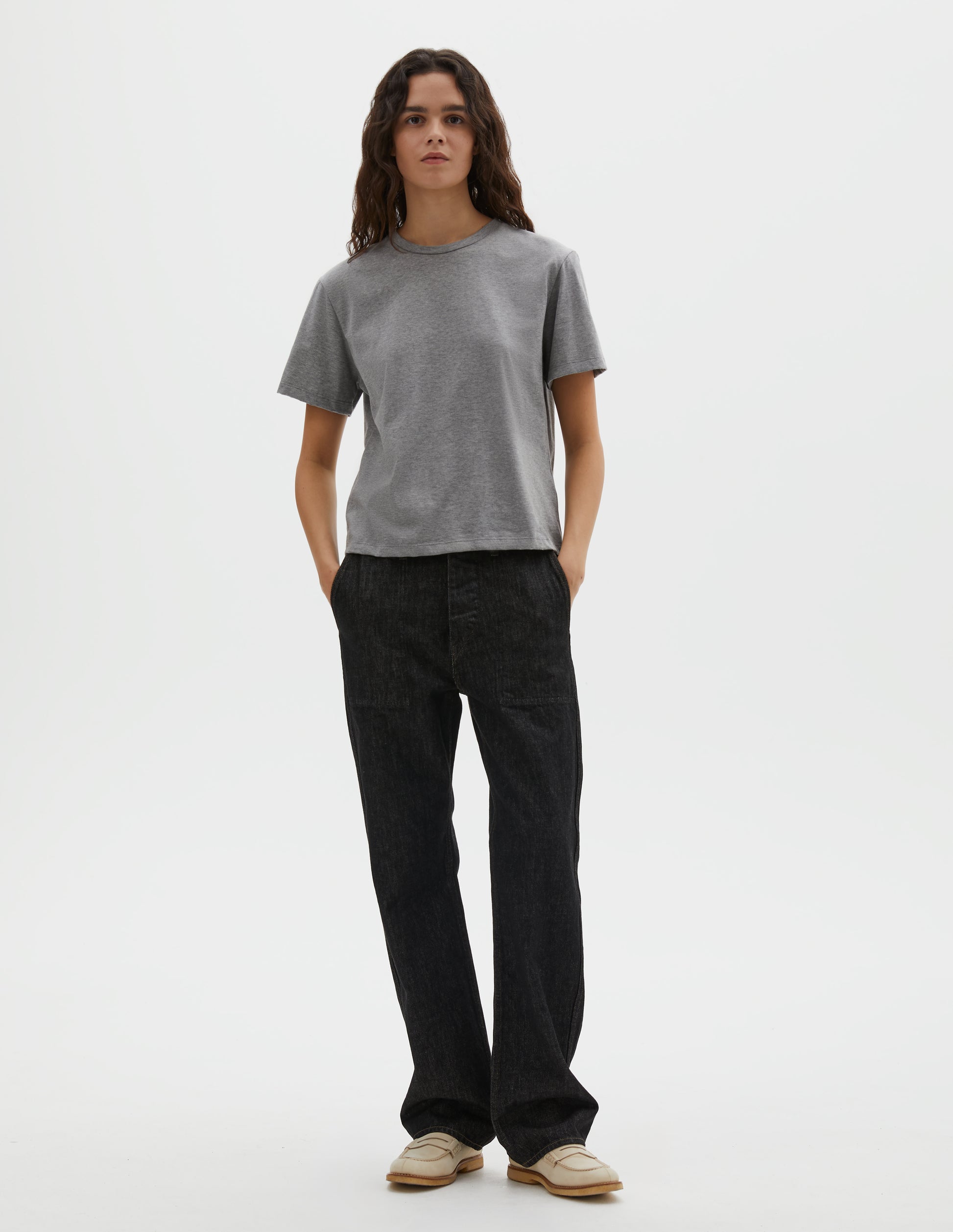 Full body image, front view of model wearing grey cotton short sleeve t-shirt with boxy cut. Styled with black denim jeans and beige suede loafers.
