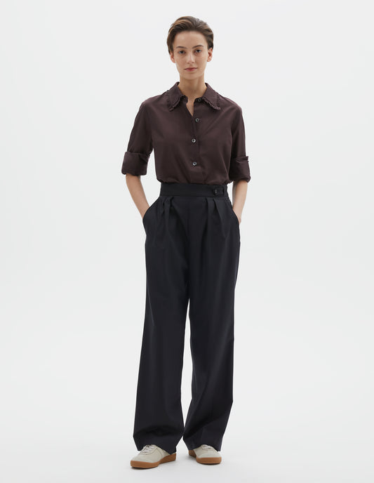 Full body image, front view of model wearing dark navy summer wool trousers with double pleats, concealed side zip, pull through double tab side fastening and slant side pockets. Styled with brown shirt and beige trainers.