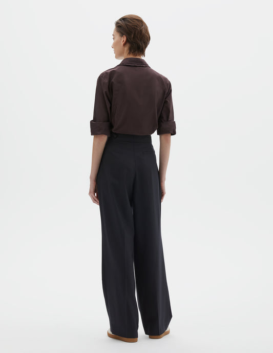 Full body image, back view of model wearing dark navy summer wool trousers with pull through double tab side fastening and back pocket. Styled with brown shirt and beige trainers.