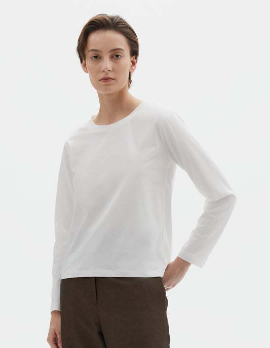 Cropped body image, front view of model wearing off white cotton wide neck long sleeve with boxy cut. Styled with brown trousers.