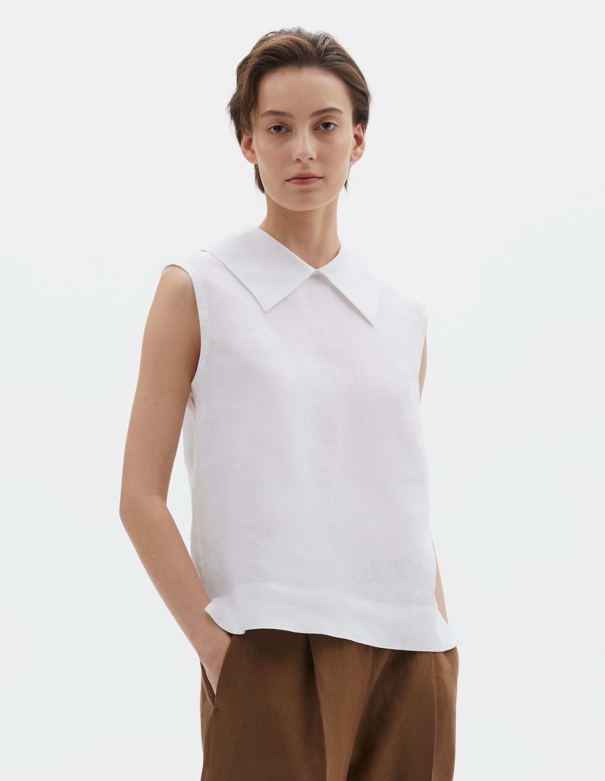 Cropped body image, front view of model wearing white regular cut Irish linen top with exaggerated collar, side dart detailing, with a deep hem with side splits. Styled with brown trousers.