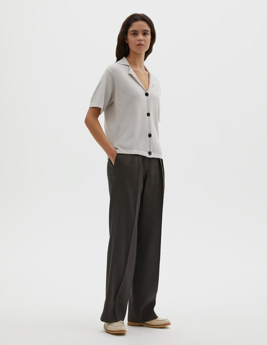 Full body image, front view of model wearing greenish brown linen silk trousers with double pleats, concealed side zip, pull through double tab side fastening and slant side pockets. Styled with off white knitted shirt and beige shoes.