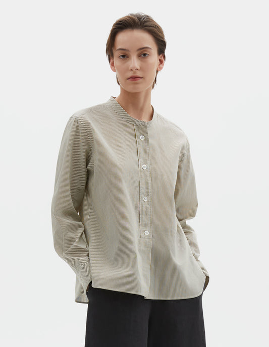 Cropped body image, front view of model wearing green and white striped cotton silk collarless shirt, with raised placket with box stitch detailing and horn button closure. Styled with black culotte trousers.