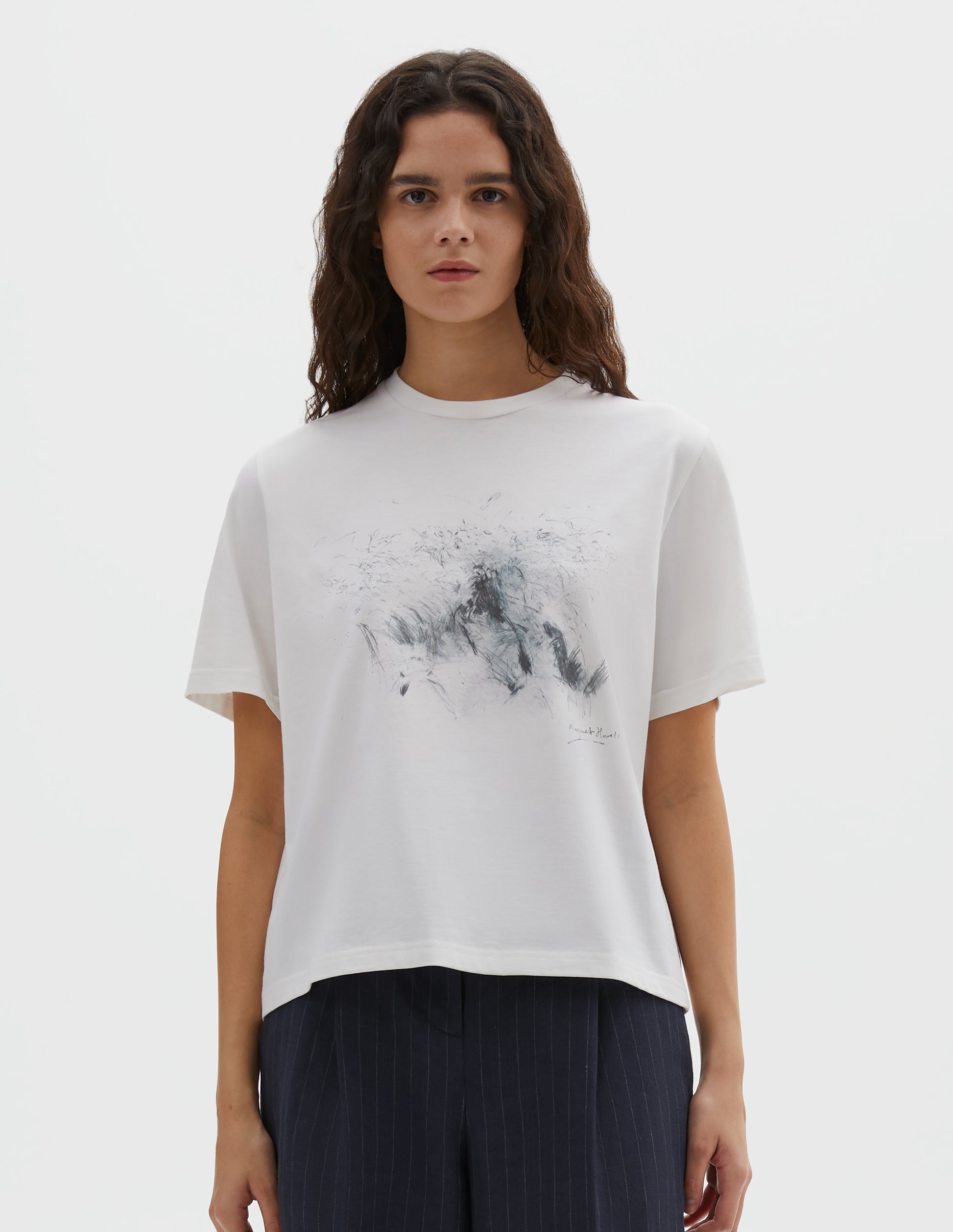 Cropped body image, front view of model wearing white relaxed, boxy crew neck t-shirt with dark grey drawing print. Styled with dark blue striped trousers.