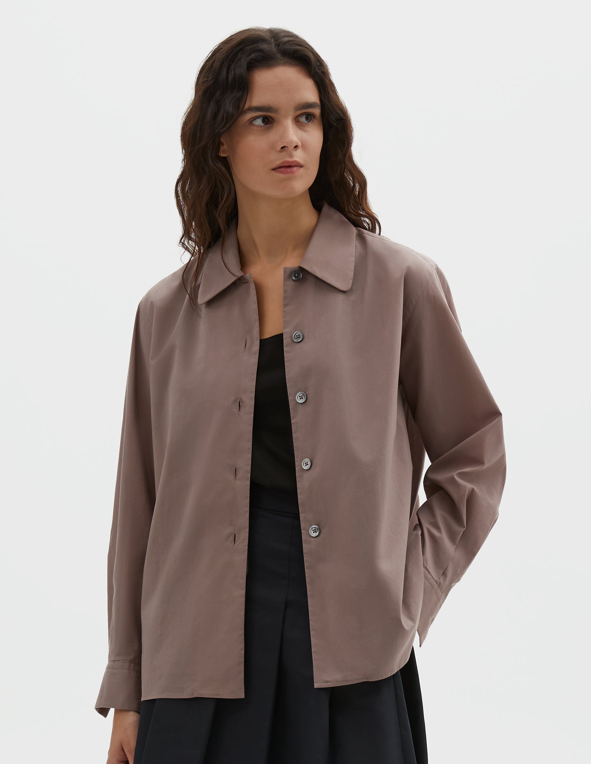 Cropped body image, front view of model pinkish brown shirt with a curved collar, side split hem. Styled over black t-shirt with blue skirt.