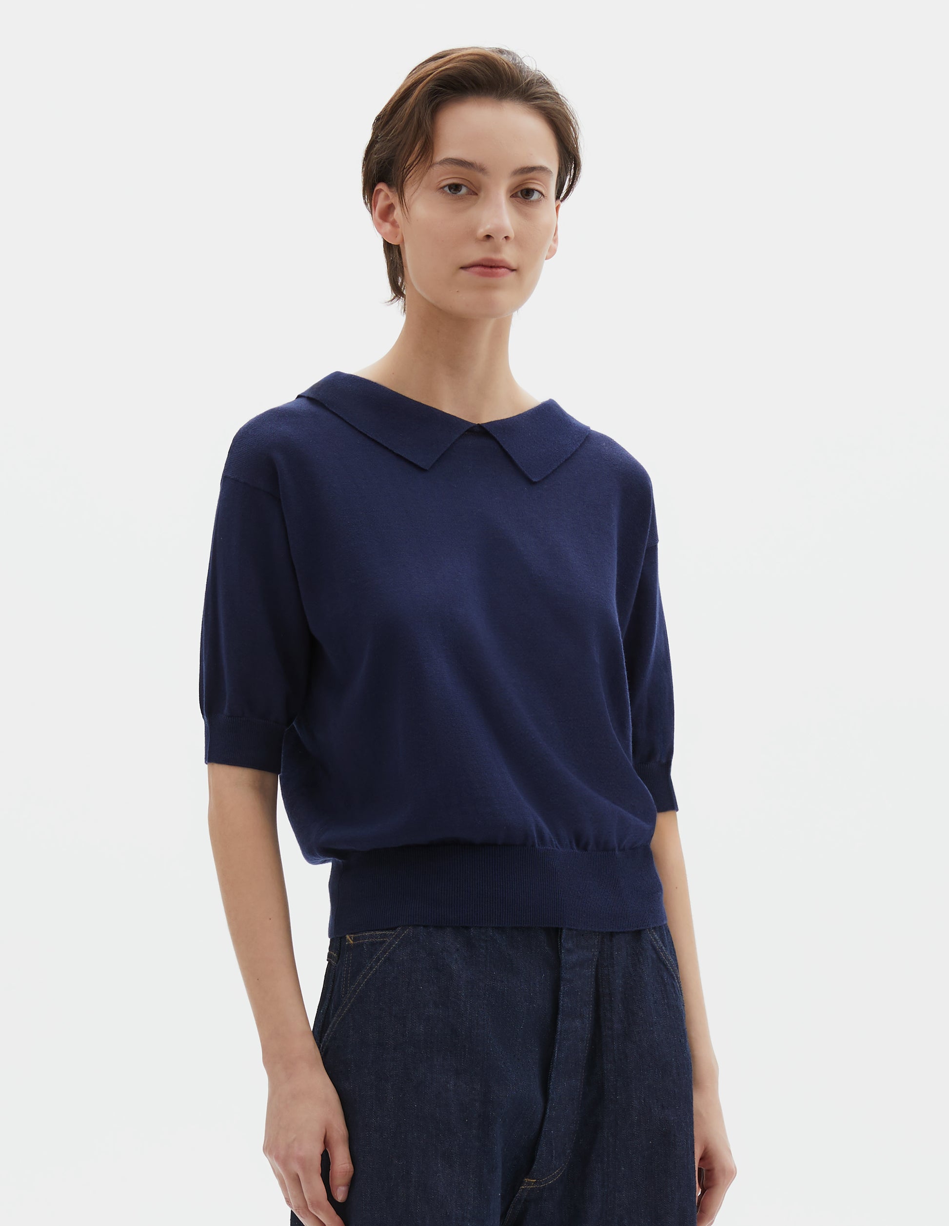 Cropped body image, front view of model wearing dark navy cotton and linen knitted t-shirt, with cutaway collar and rib cuff and hem. Styled with indigo blue denim shorts.