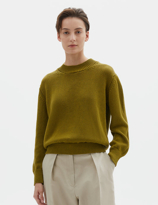 Cropped body image, front view of model wearing greenish yellow linen and cotton crew neck jumper, with deep rib crew neck, rib cuffs and hem. Styled with beige linen trousers.