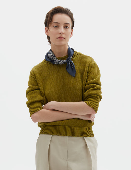 Cropped body image, front view of model wearing a navy blue bandana. Styled with a yellowish green jumper and beige pleated trousers.