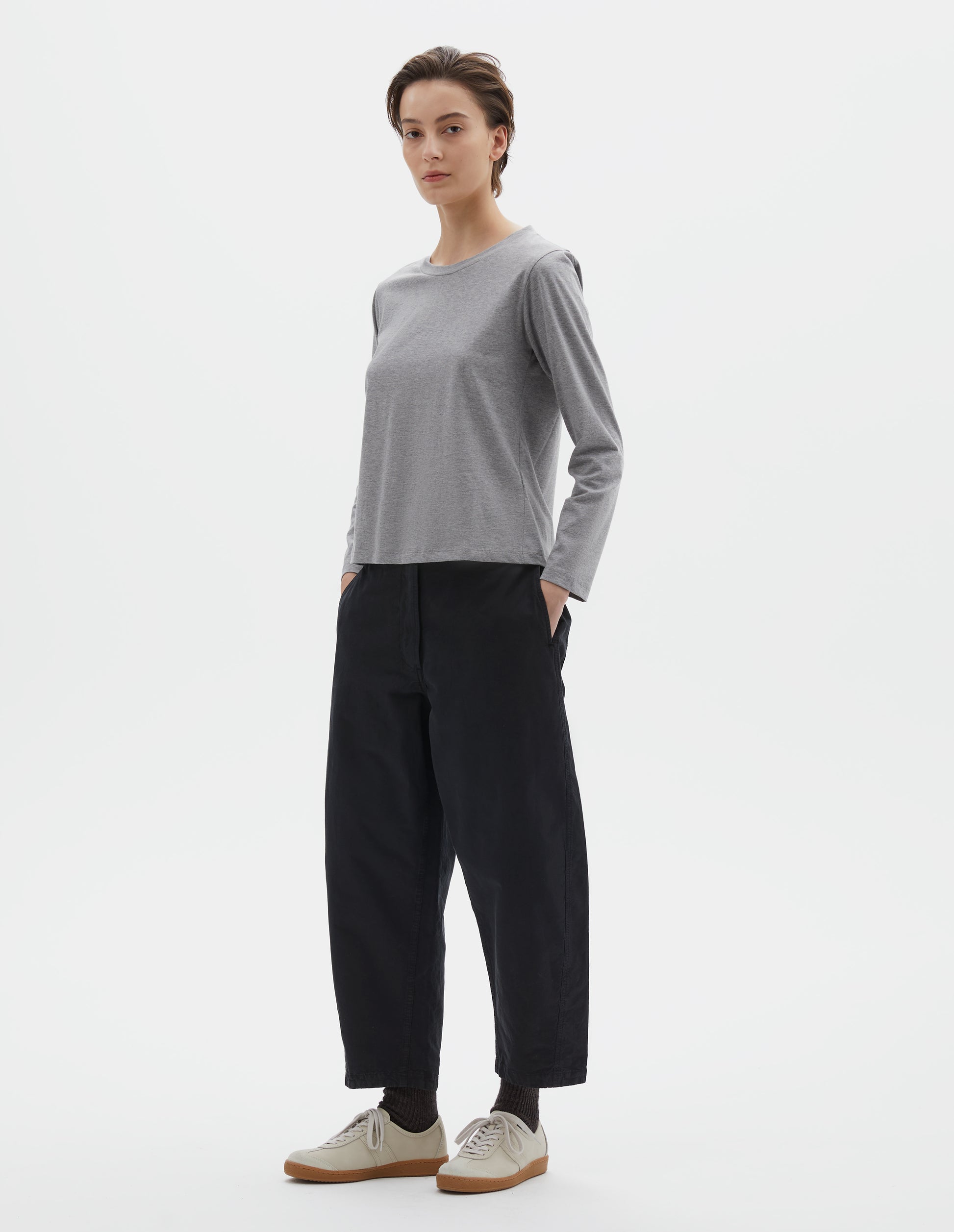 Full body image, front view of model wearing grey cotton wide neck long sleeve with boxy cut. Styled with black cropped trousers, black socks and beige suede trainers.