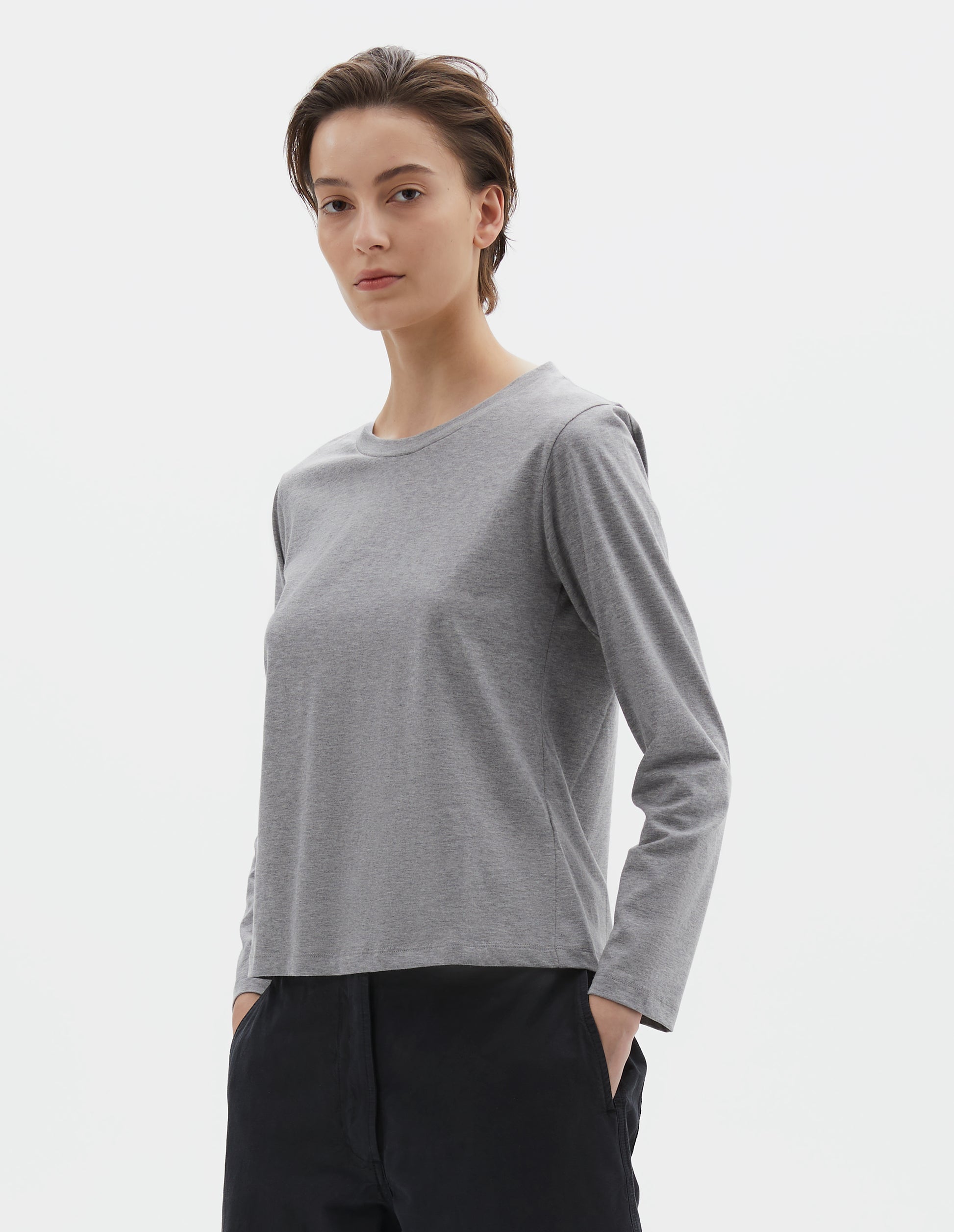 Cropped body image, front view of model wearing grey cotton wide neck long sleeve with boxy cut. Styled with black cropped trousers.