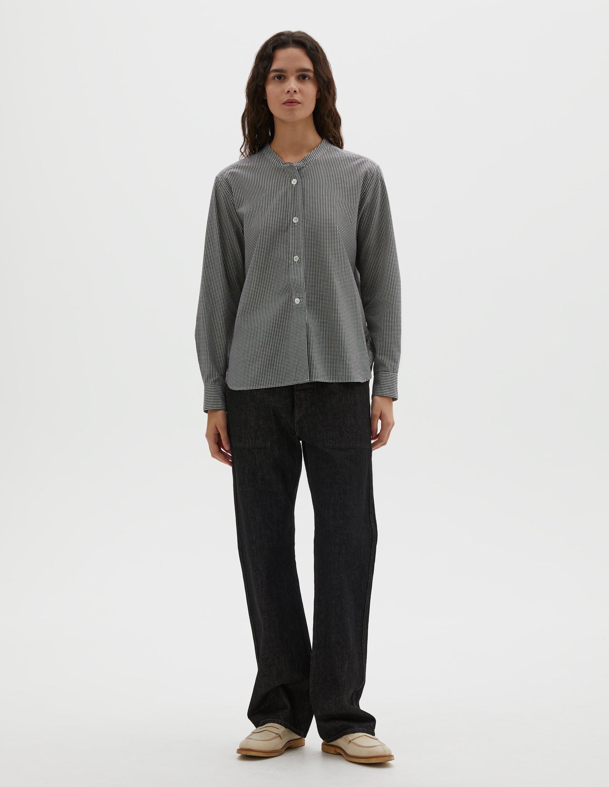 Full body image, front view of model wearing black and white gingham cotton cashmere collarless long sleeve shirt, with raised placket and mother of pearl buttons. Styled with black denim jeans and beige loafers.