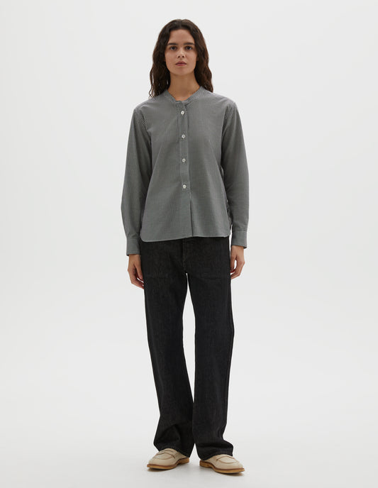 Full body image, front view of model wearing black and white gingham cotton cashmere collarless long sleeve shirt, with raised placket and mother of pearl buttons. Styled with black denim jeans and beige loafers.