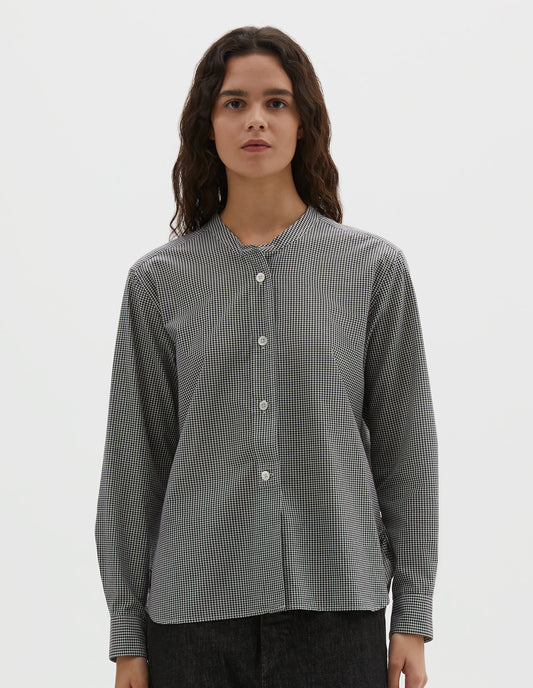 Cropped body image, front view of model wearing black and white gingham cotton cashmere collarless long sleeve shirt, with raised placket and mother of pearl buttons. Styled with black denim jeans.