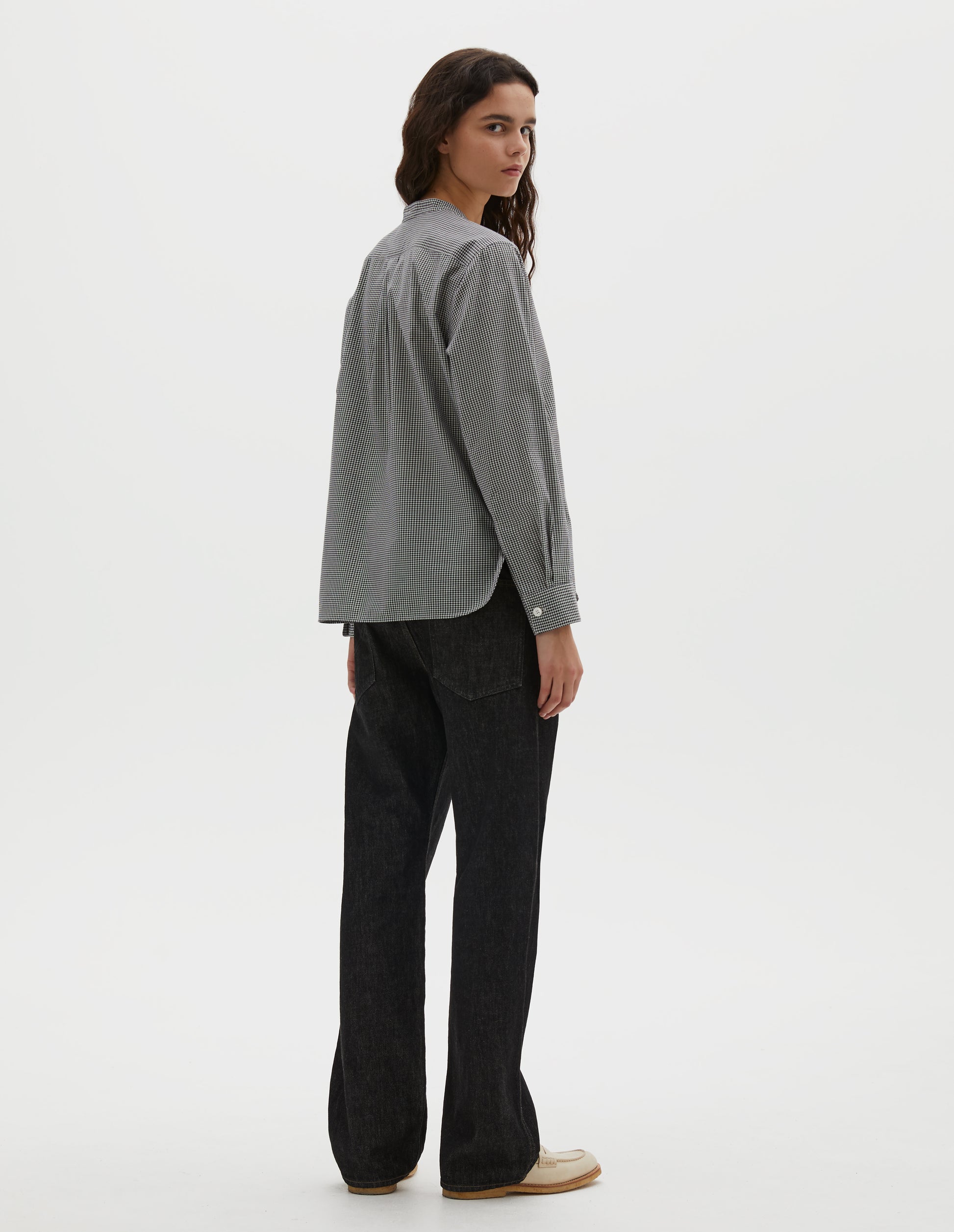 Full body image, back view of model wearing black and white gingham cotton cashmere collarless long sleeve shirt, with mother of pearl button cuffs, box stitch detailing on back yoke and elongated hem. Styled with black denim jeans and beige loafers.