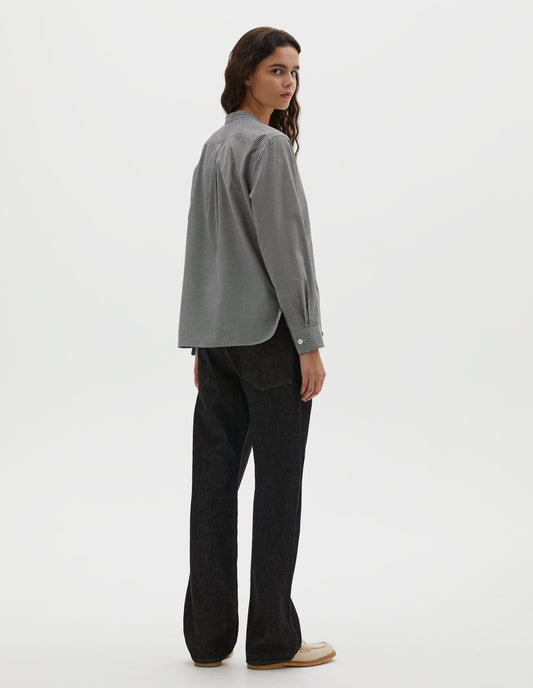 Full body image, back view of model wearing black and white gingham cotton cashmere collarless long sleeve shirt, with mother of pearl button cuffs, box stitch detailing on back yoke and elongated hem. Styled with black denim jeans and beige loafers.