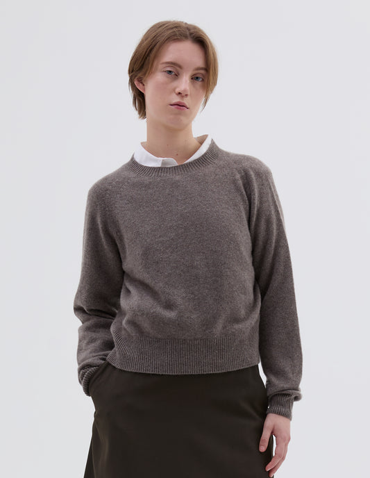 Cropped body image, front view of model wearing greyish beige jumper with raglan sleeve, contrast rib on neck, cuffs and hem. Styled over white shirt, with brown skirt.