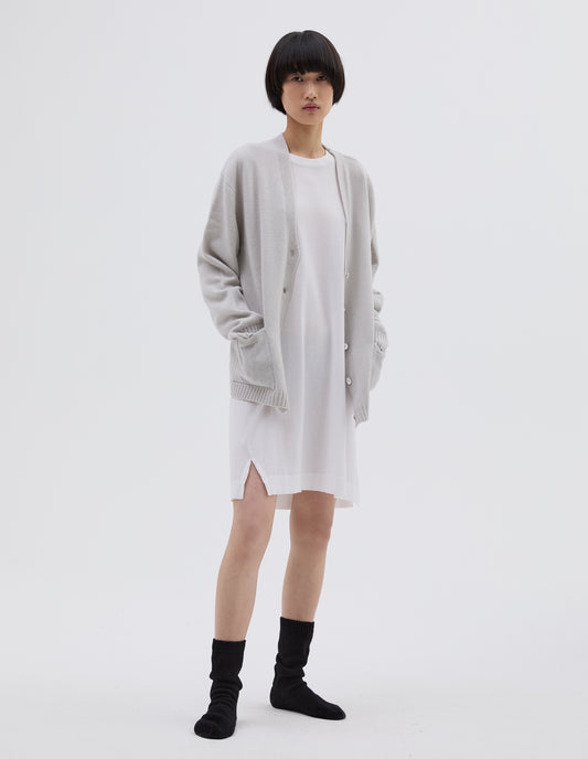 Full body image, front view of model wearing light grey merino cashmere bed cardigan, with contrast rib on neck, cuff and hem and front patch pockets. Styled with white cotton night t shirt and black bed socks.