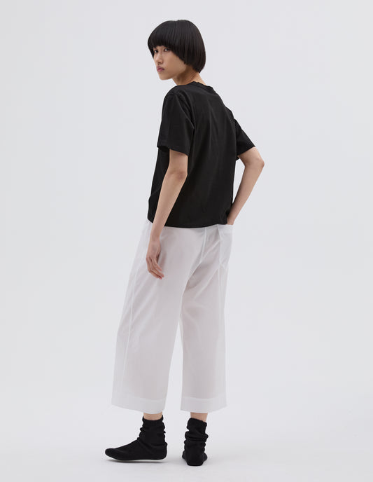 Full body image, back view of model wearing white lightweight cotton cropped PJ pants with gathered back and patch back pocket. Styled with black t-shirt and black bed socks.
