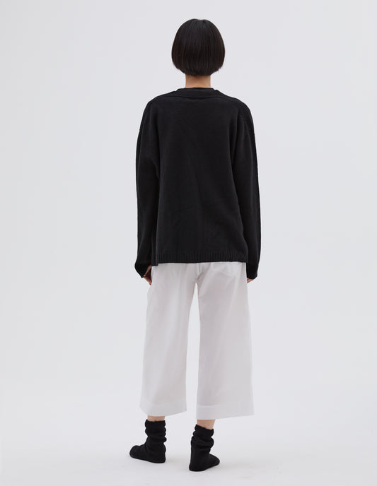 Full body image, back view of model wearing black merino cashmere bed cardigan, with contrast rib on neck, cuff and hem. Styled with white cotton PJ pants and black bed socks.