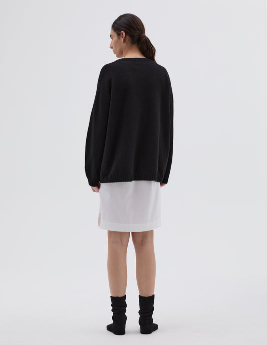 Full body image, back view of model wearing black merino cashmere bed jumper with raglan sleeve and contrast rib on neck, cuffs and hem. Styled with white cotton night t shirt and black bed socks.