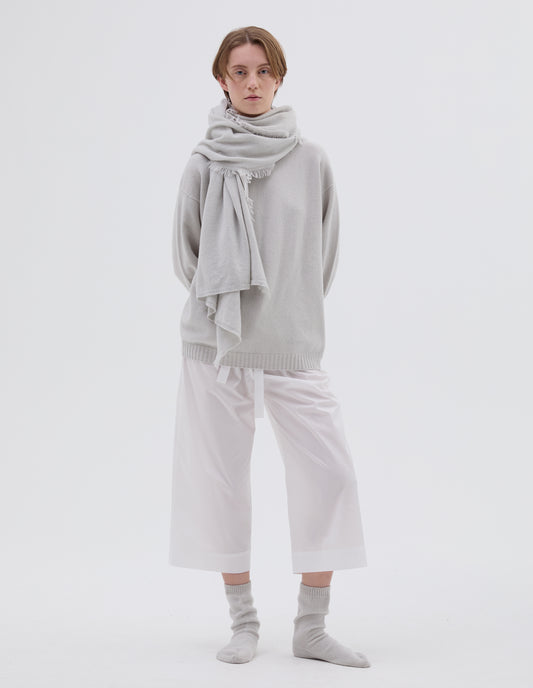 Full body image, front view of model wearing light grey merino wool and cashmere bed shawl, Styled with light grey jumper, white cotton trousers and light grey bed socks.