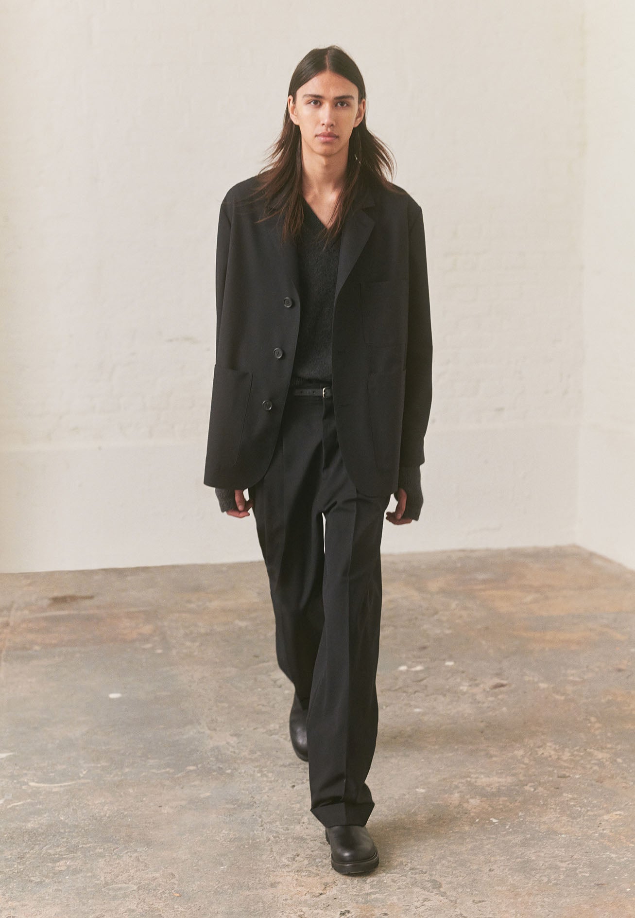 Full body image, front view of model wearing charcoal grey sleeveless knitted jumper, with contrast rib on neck, armholes and hem. Styled with black blazer, matching trousers and black leather boots.