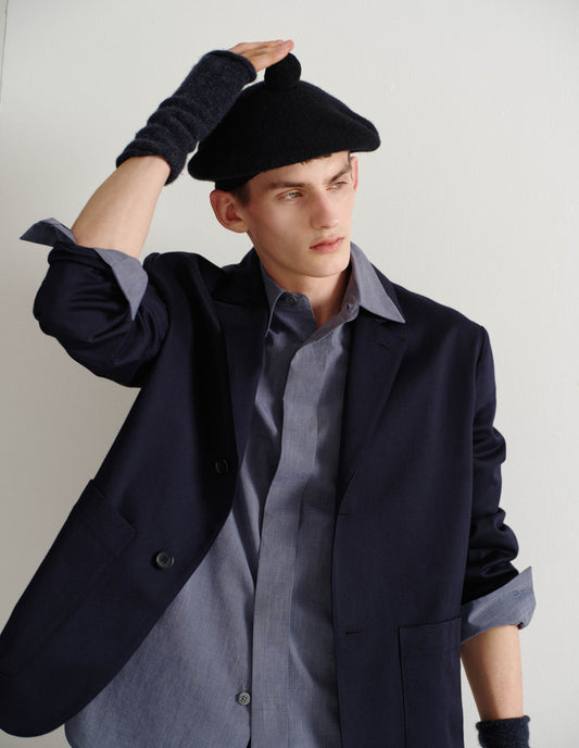 Cropped body image, front view of male model wearing dark blue merino cashmere fingerless mittens with contrasting blue and grey flecks. Styled with black beret and dark blue blazer over blue shirt with sleeves rolled up.