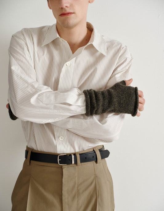 Cropped body image, front view of male model wearing dark green merino cashmere fingerless mittens with contrasting green and grey flecks. Styled with striped white shirt, black leather belt and beige trousers.