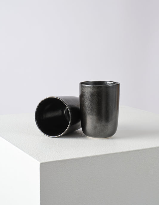 A pair of tall black beakers, one on its side so you can see the fully glazed inner.